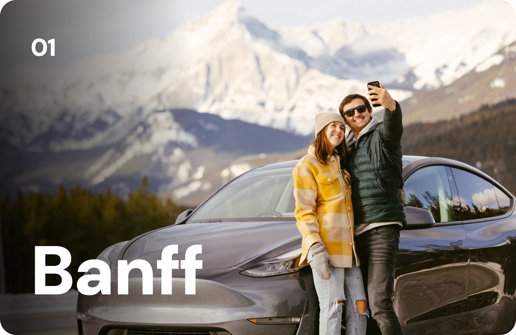 A man and woman take a selfie beside their car in the mountains. 01 Banff
