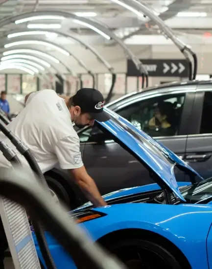 Man looking under the hood of a blue car in a parking garage