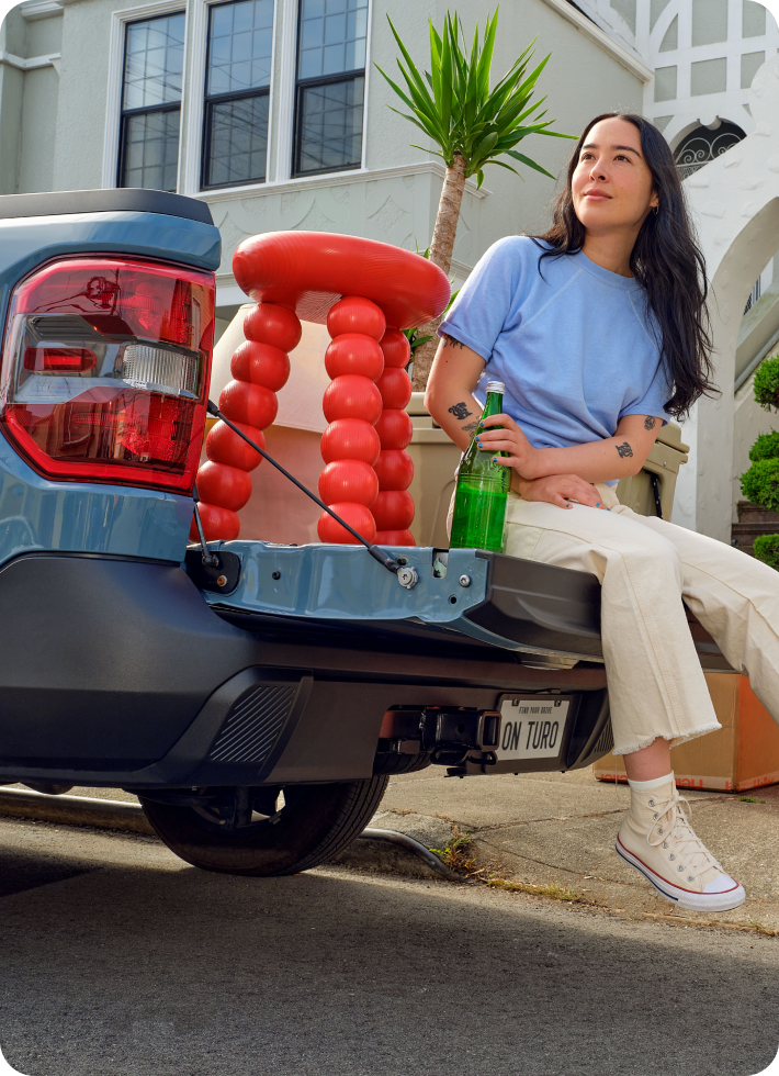 A woman with a water bottle sits on the open tailgate of a pickup truck.