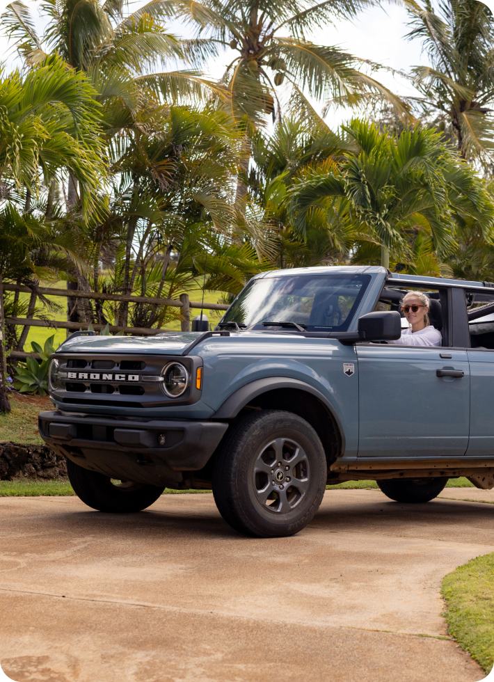 A woman drives past palm trees in a blue SUV.