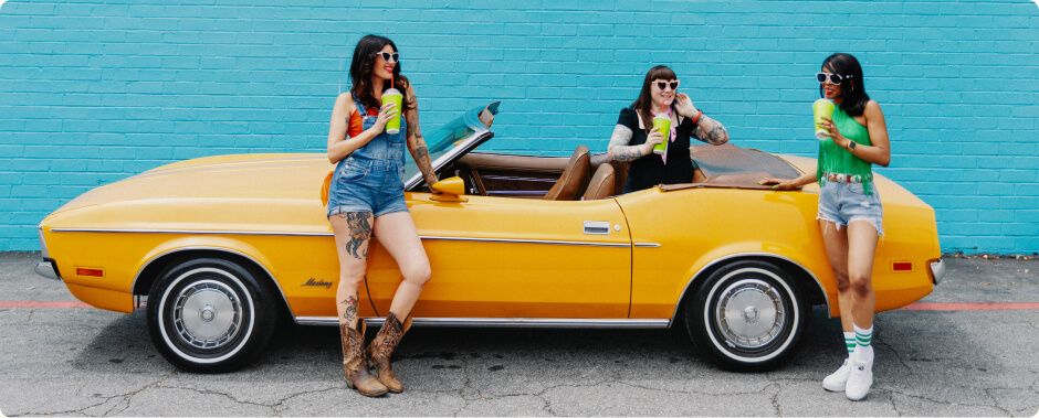Yellow classic Mustang and three women in front of blue wall