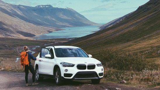 Voyageur debout près d’un SUV devant un lac entouré de montagnes