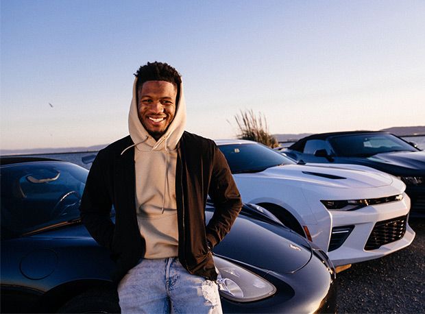 Turo host smiling, with hands in jacket pockets, leaning against one of his three vehicles at the Port of Oakland