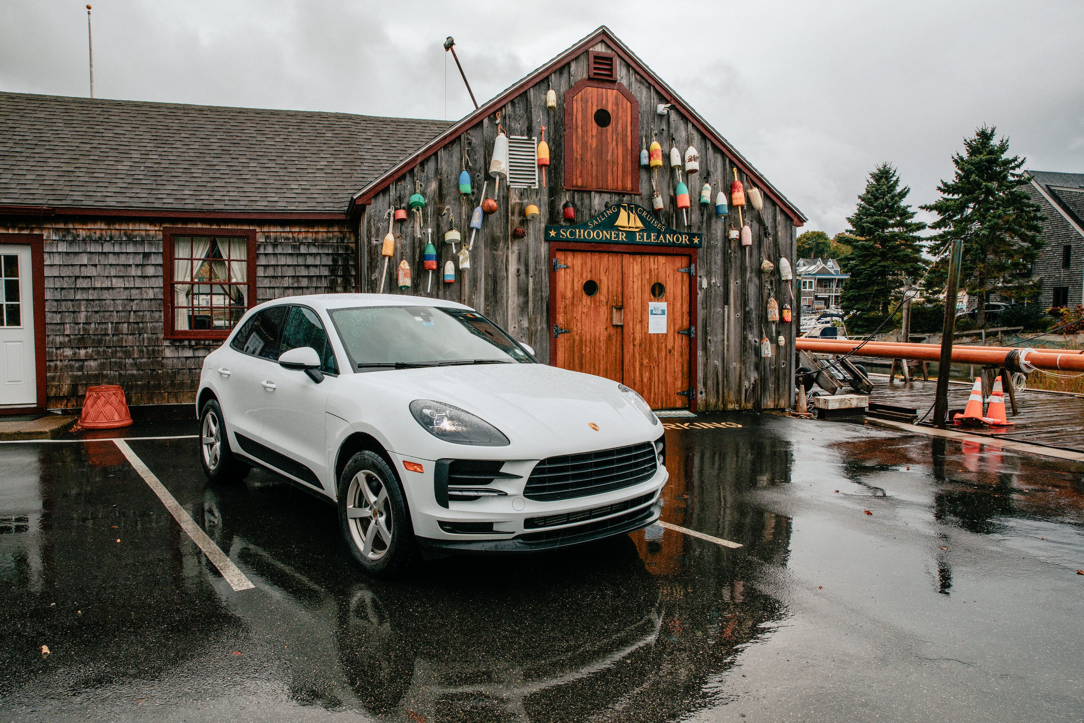 White SUV parked on wet pavement by a buoy-covered waterfront building near Boston