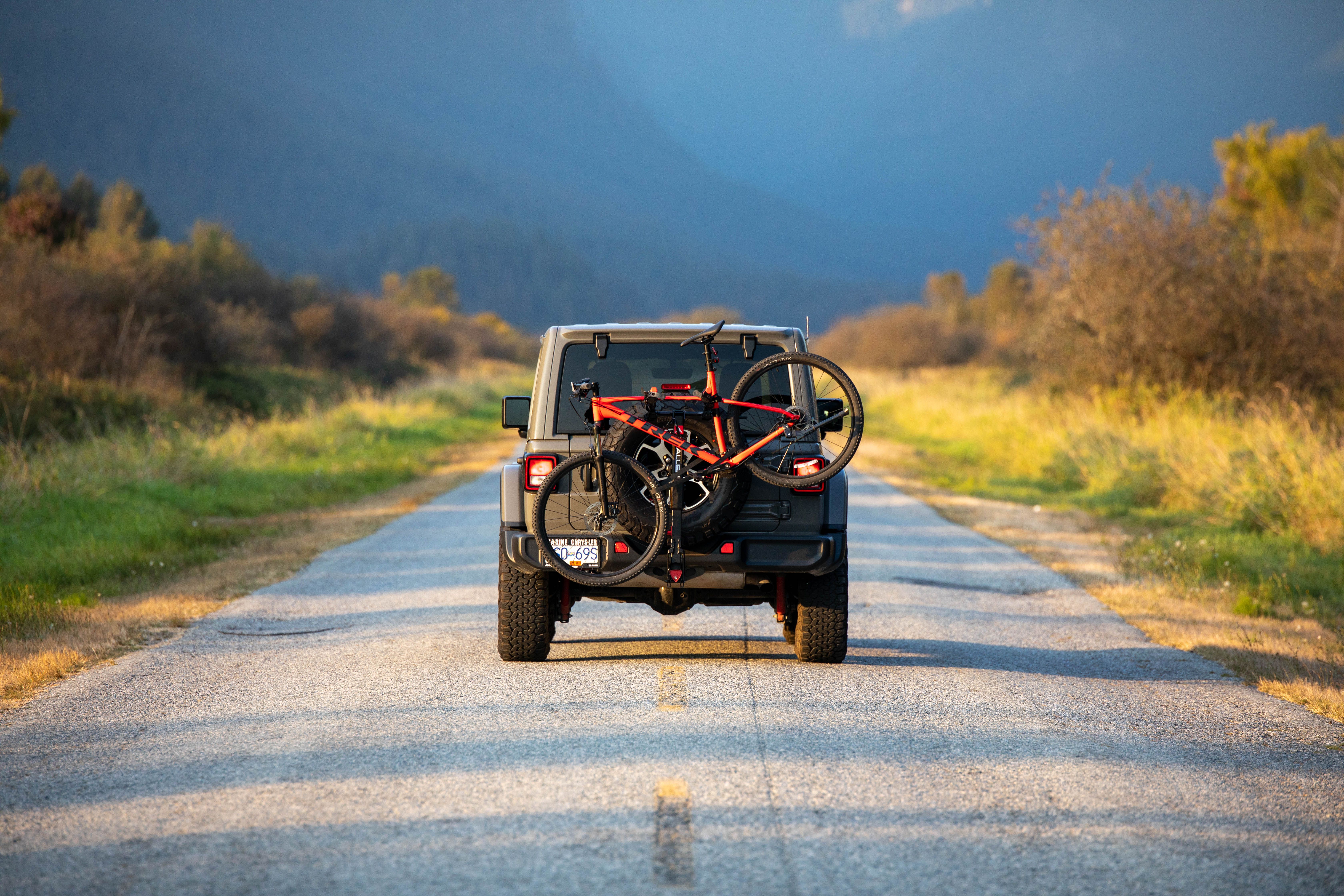 SUV with a mountain bike on the back driving along a sunlit rural road