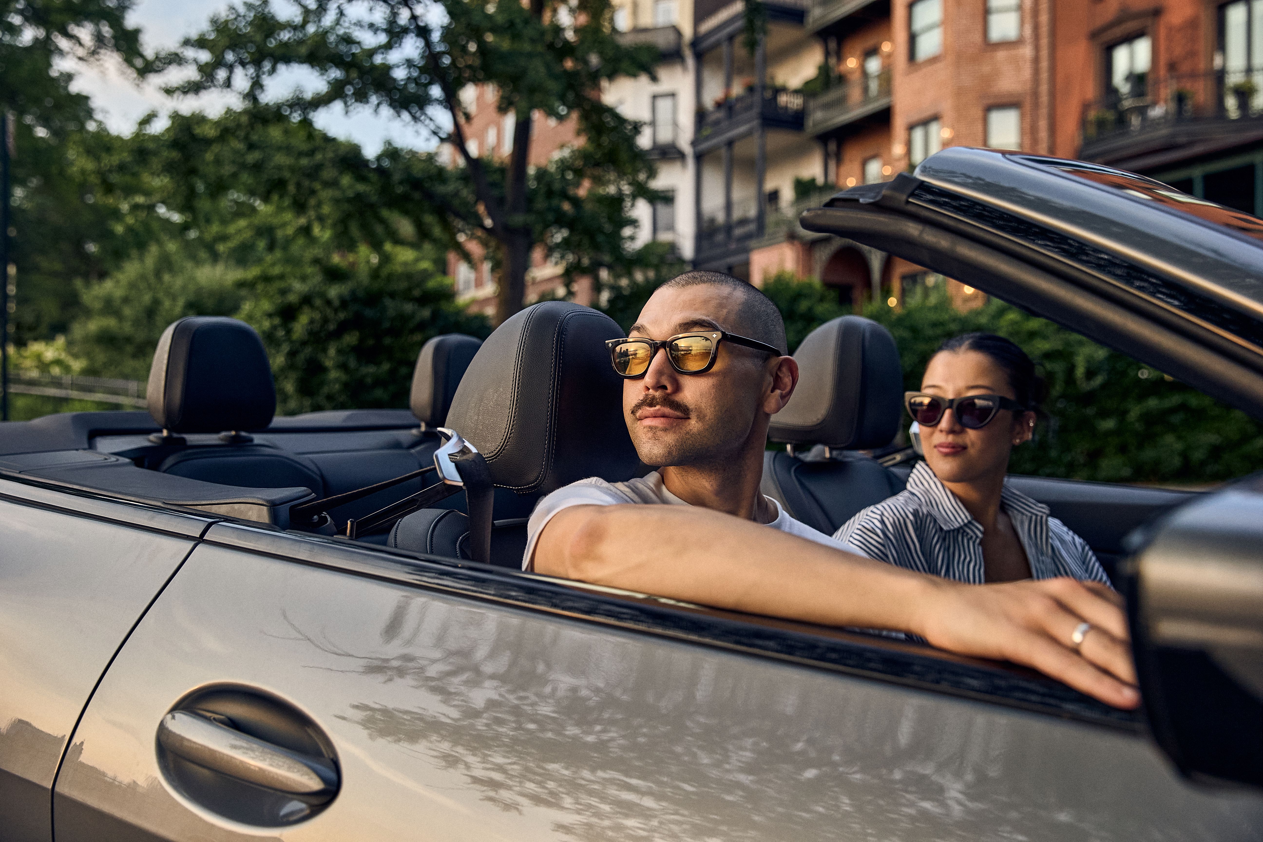 People ride in a convertible past tree-lined brick rowhouses in Washington, DC