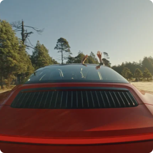 A passenger sticks their arms through the sunroof of a red sports car.