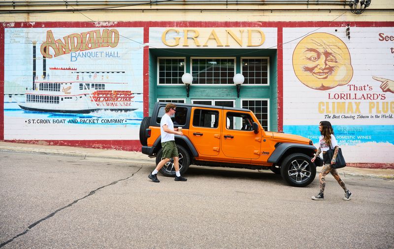 Orange Jeep Wrangler parked by colorful Grand Banquet Hall murals on a Chicago street