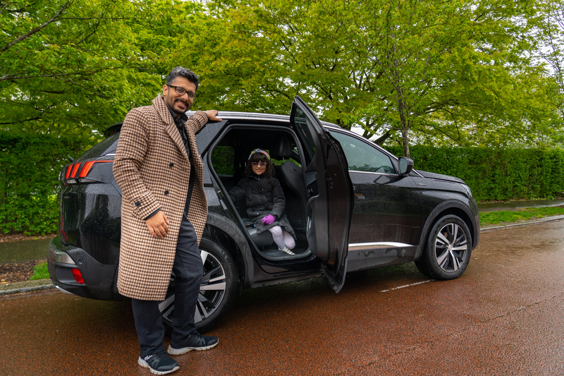 Man helping a child into a black SUV on a rainy, tree-lined road in Caen