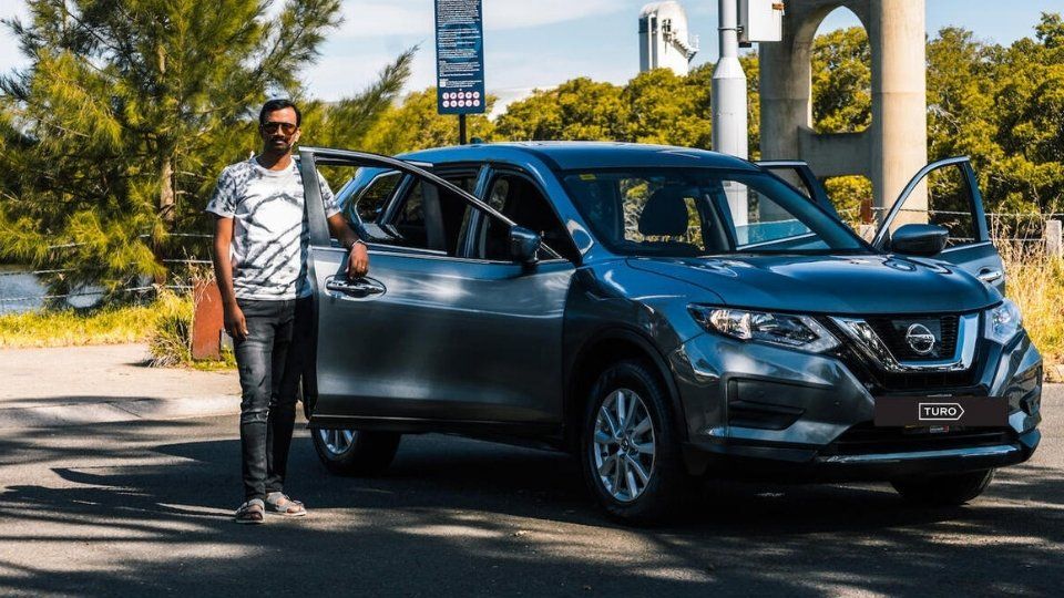 A Turo guest stands next to a Polestar rental car in Melbourne, with the beach in the background
