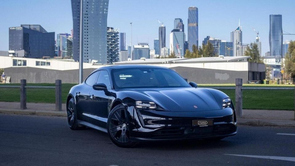 A Turo guest stands next to a Polestar rental car in Melbourne, with the beach in the background
