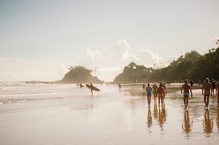 A photo of surfers walking along the beach in Byron Bay - a popular car hire destination.